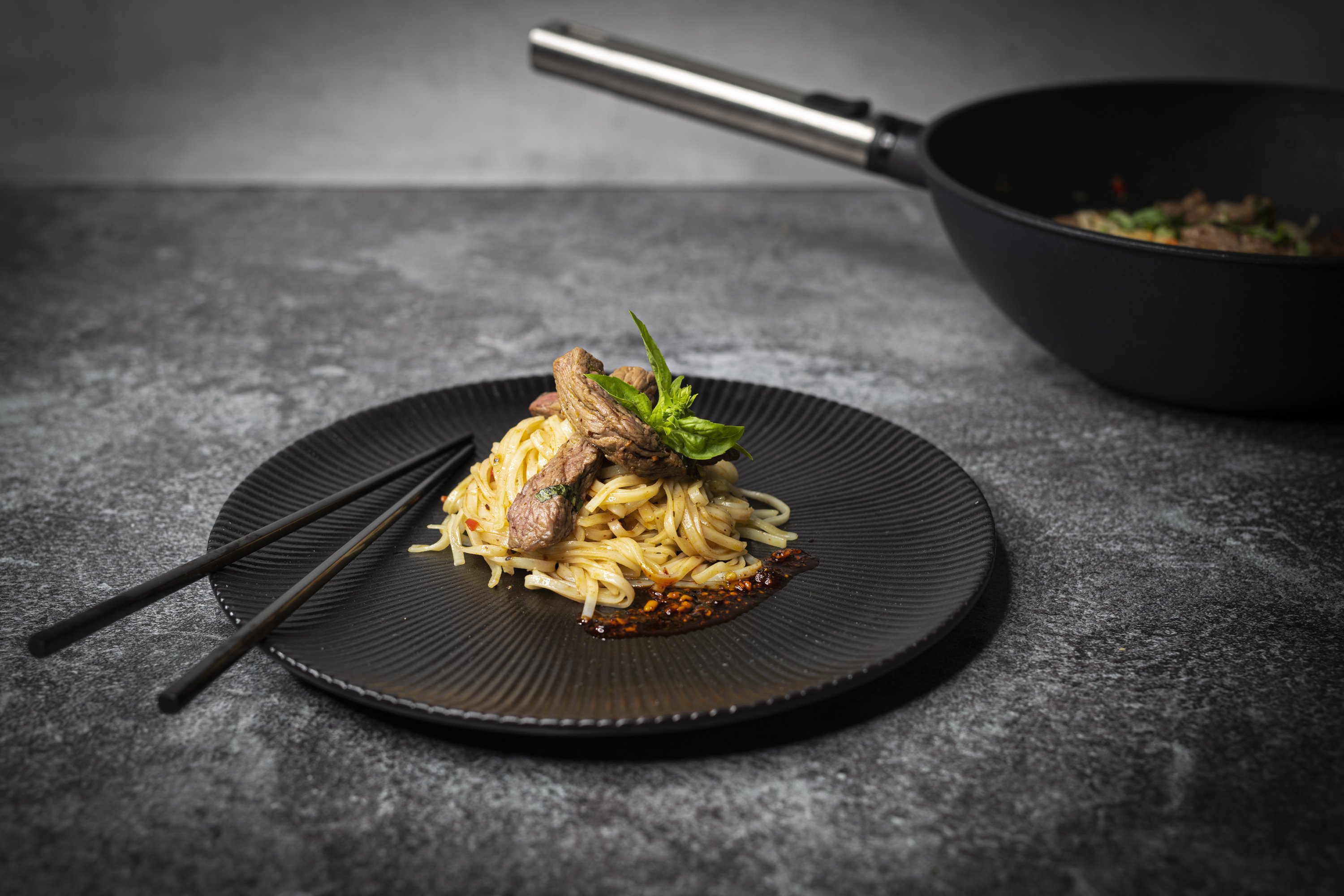 In einer runden Logic XR Wok- und Rührpfanne wurden Asia Nudeln zubereitet und auf einem Teller platziert. 