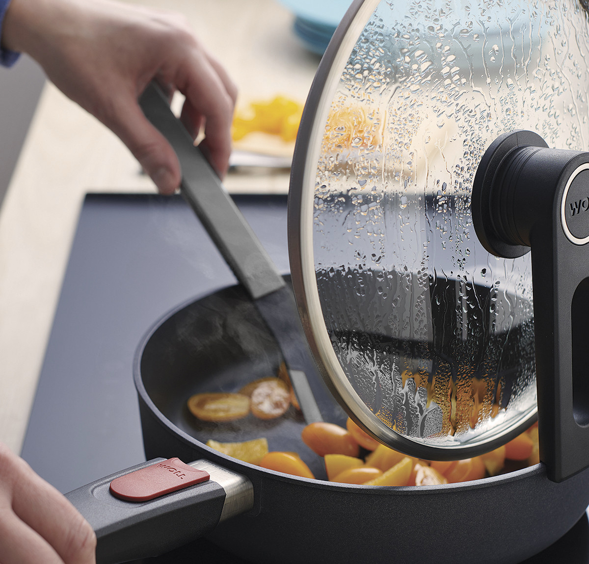 In der runden Diamond Lite Pfanne wird ein Gericht mit einem grauen Cock it Pfannenwender umgerührt. Der Smart Lid steht auf der Pfannenkante.