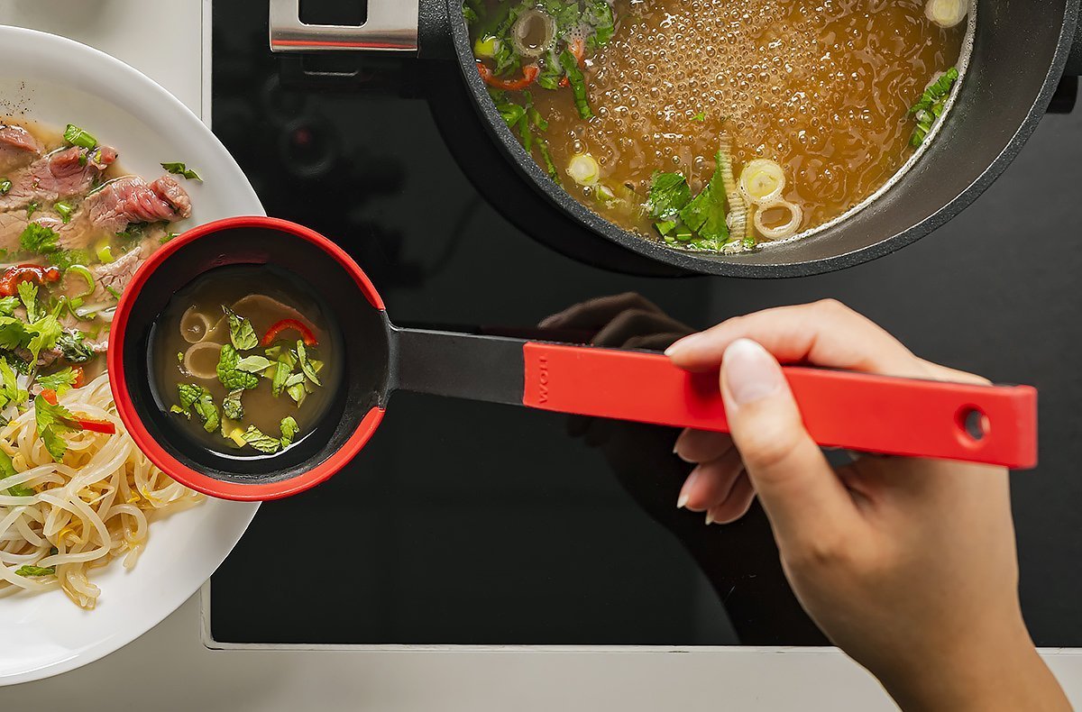 In einem runden Logic Topf befindet sich gekochte Brühe. Mit einer roten Cock it Schöpfkelle wird die Brühe über die Nudeln im Teller gegossen.