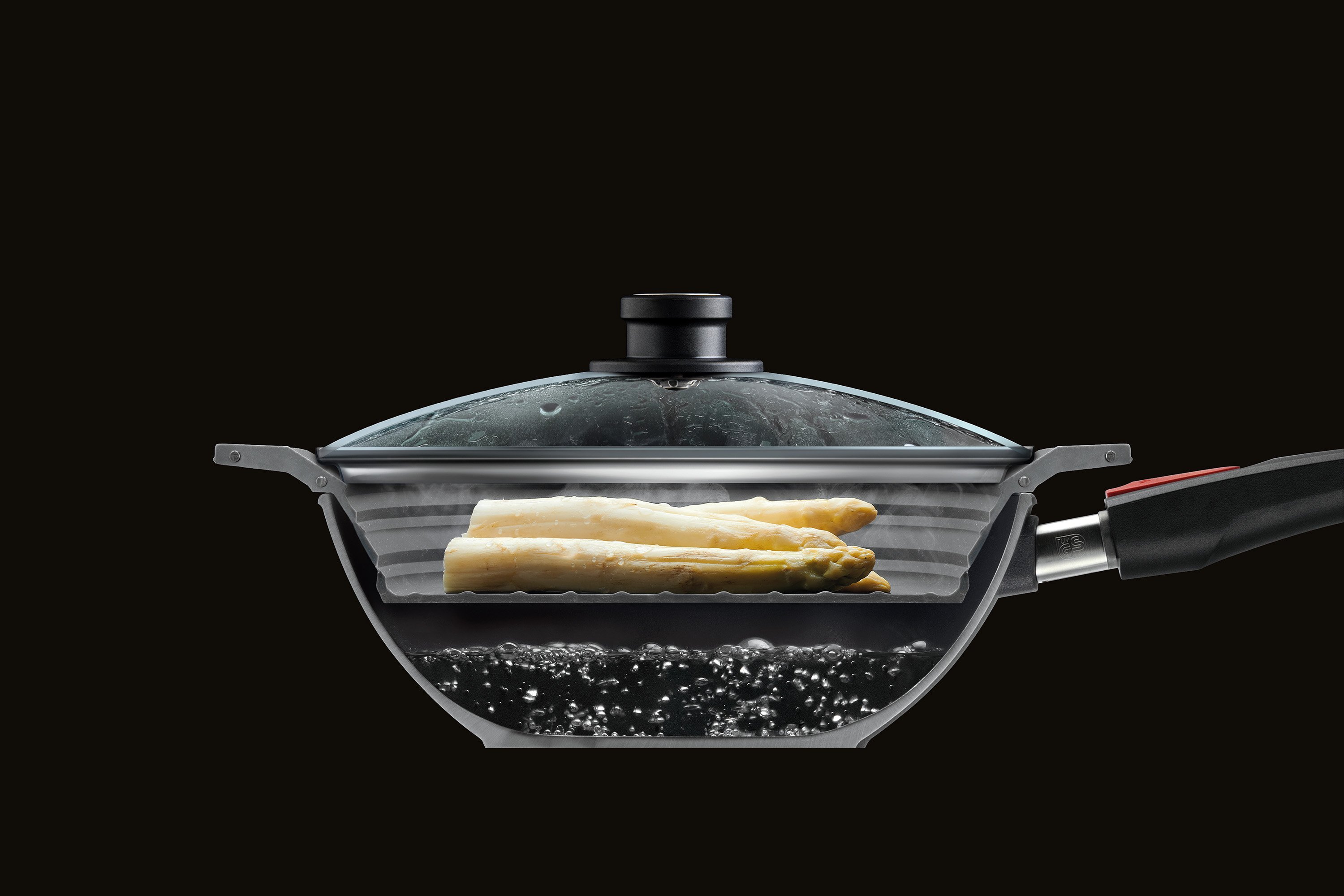 SI26F_Mood Im Querschnitt ist eine halbierte Wok Pfanne mit Glasdeckel zu sehen, in der Spargel mit dem Steam it multifunktionalen Silikoneinsatz gedämpft wird.