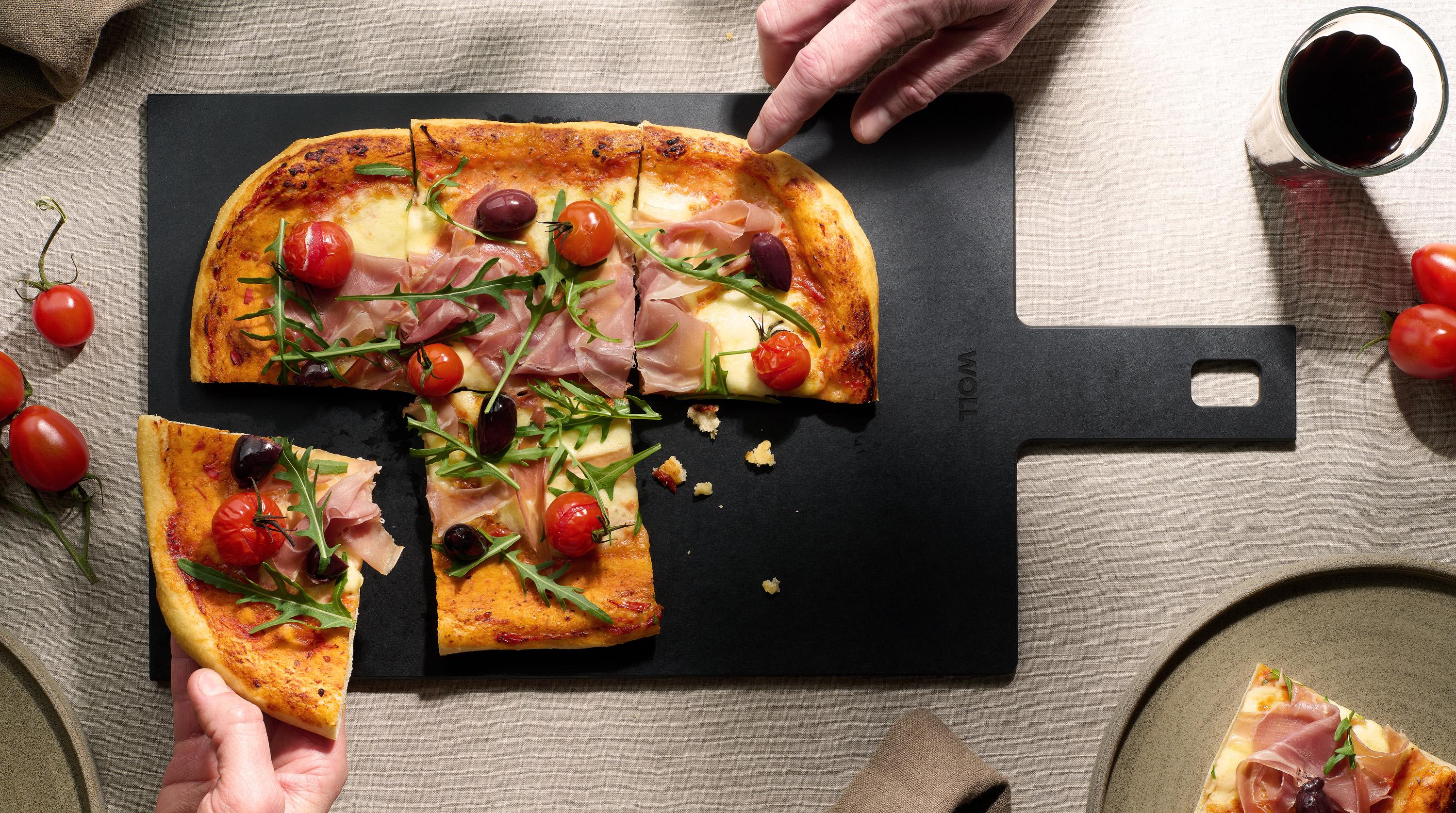 Auf dem Cut & Serve Schneidebrett mit Griff  liegen frisch gebackene Pizzastücke. 