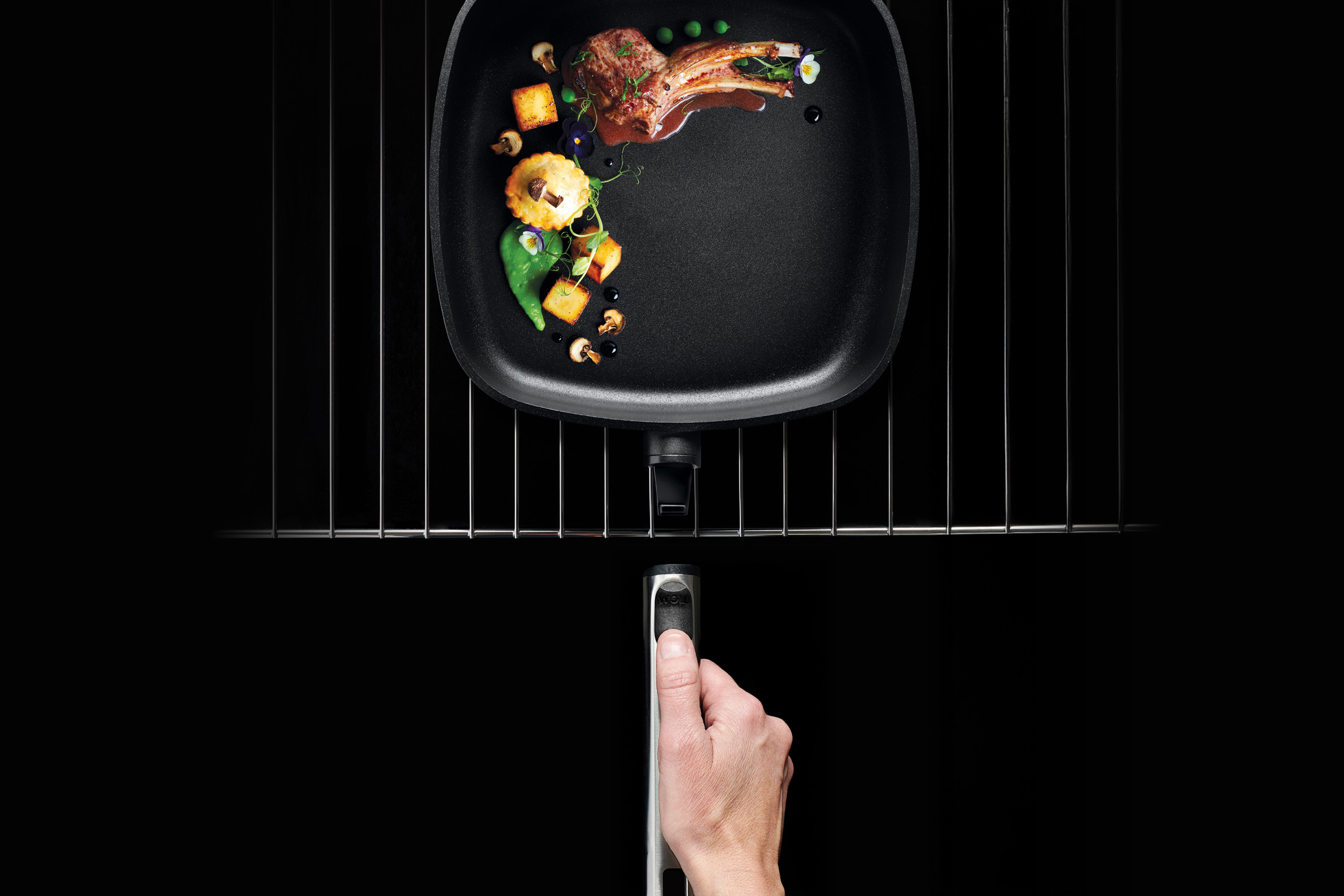 Auf dem Rost steht eine viereckige Logic XR Pfanne, in dieser befindet sich ein angerichtetes Fleischgericht. 