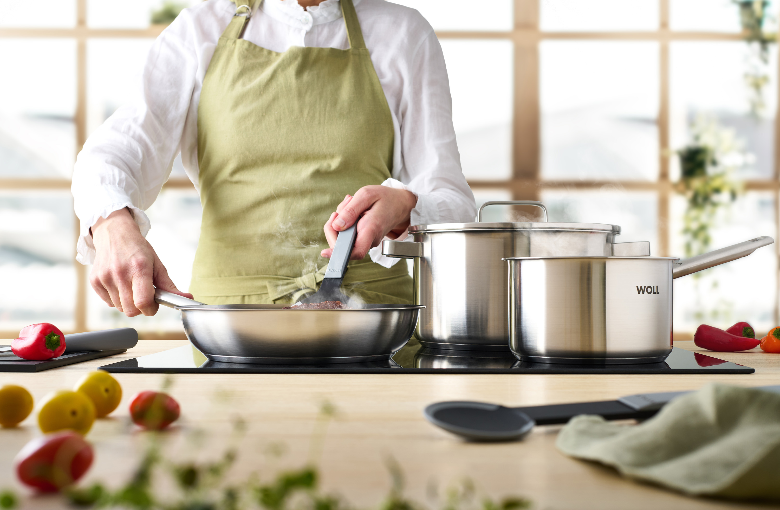 In einer Steel Pfanne wird Fleisch angebraten und gewendet. Zwei weitere Steel Töpfe stehen auf dem Herd.