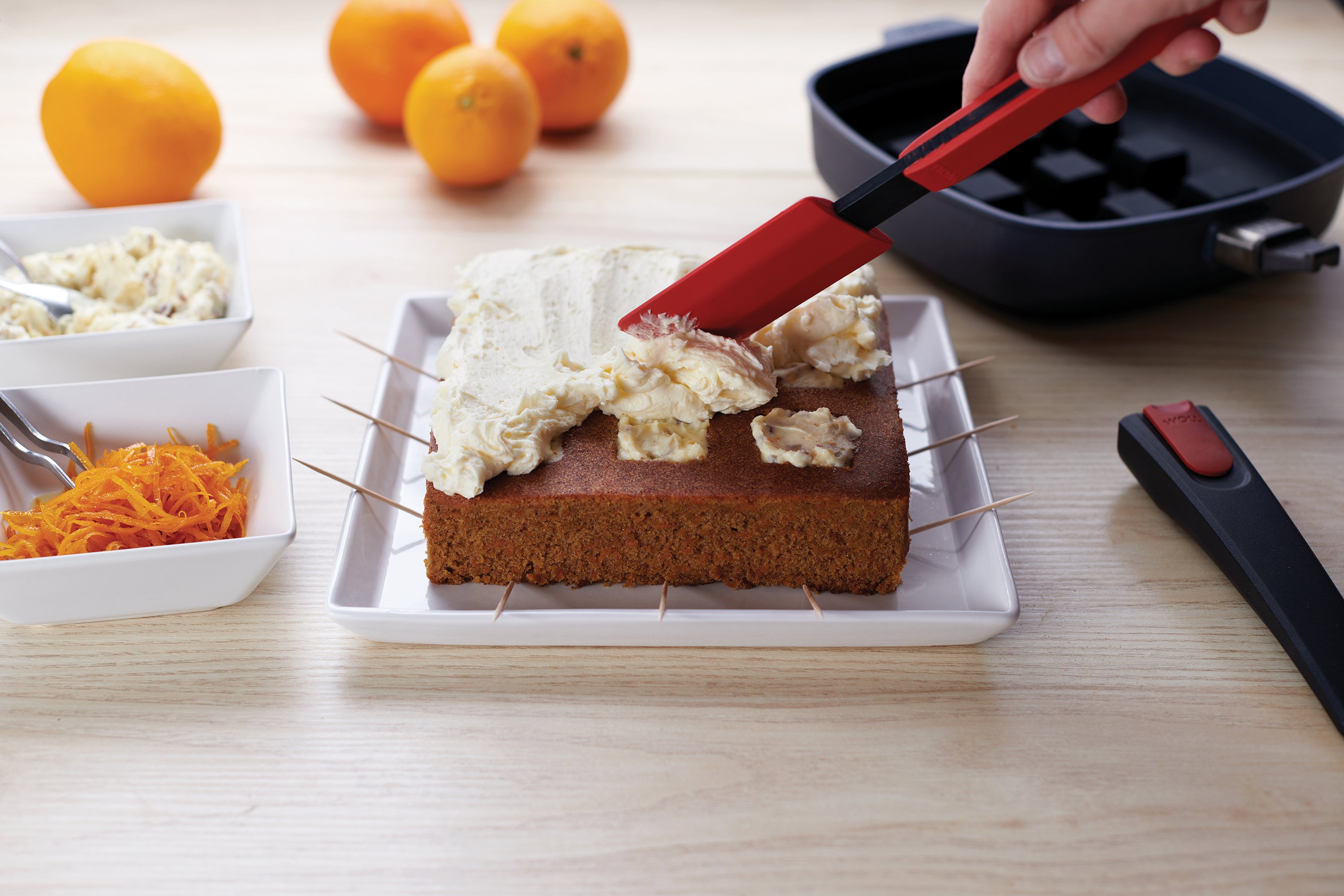 Mit dem Cock it Teigschaber wird die Creme auf dem frisch gebackenen Kuchen verteilt. Daneben steht eine Diamond Lite Pfanne mit Silikon-Backeinsatz.