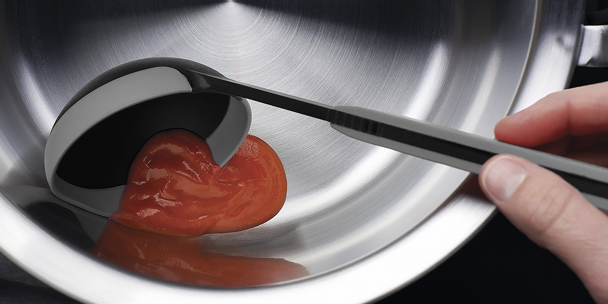 Die Tomatensoße wird mithilfe der grauen Cock it Schöpfkelle in eine silberne Schüssel gegeben.