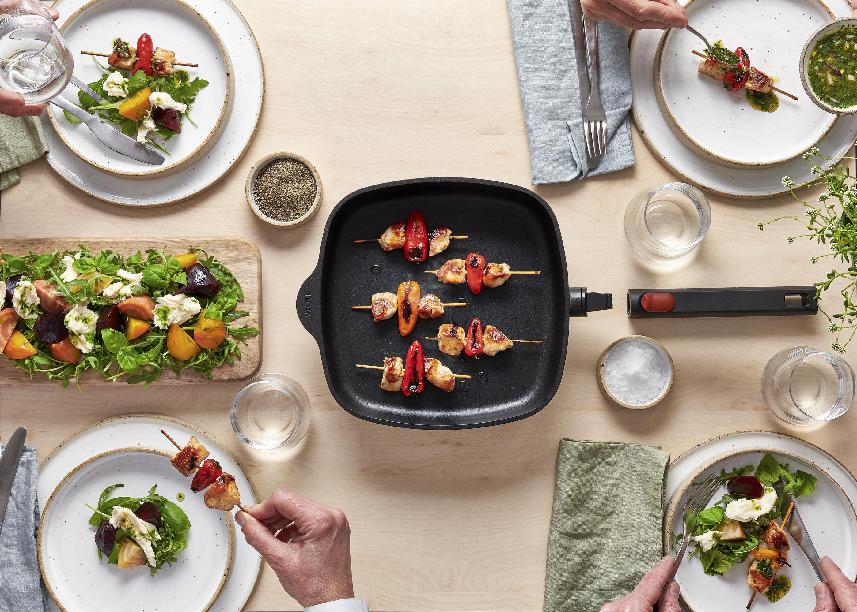 Auf dem Tisch steht eine viereckige Eco Logic QXR Pfanne, in der sich angebratene Fleischspieße befinden.