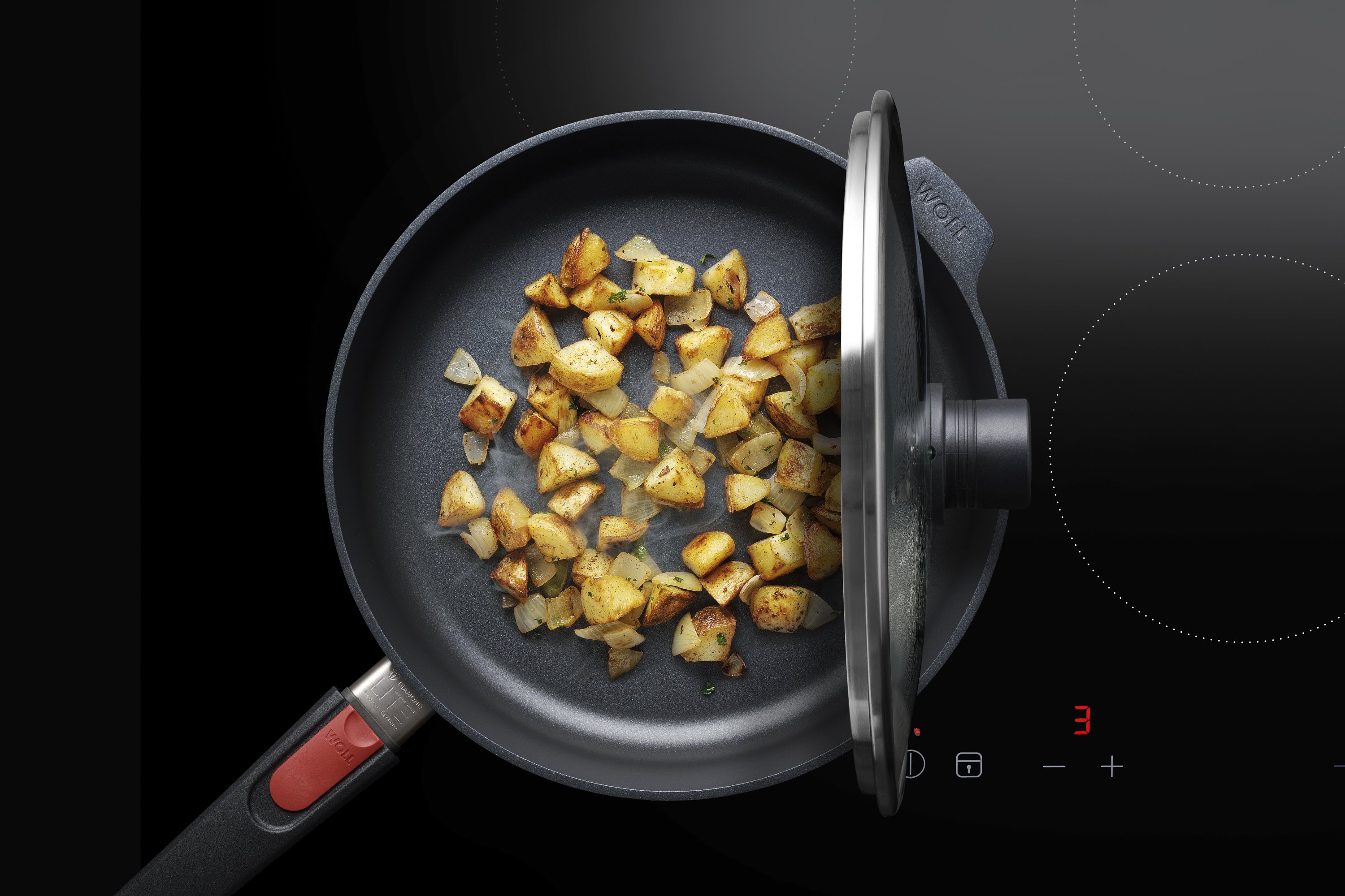 Auf dem Herd steht eine runde Diamond-Lite-Pfanne, in der ein Gericht zubereitet wird. Der Smart Lid steht auf der Pfannenkante.