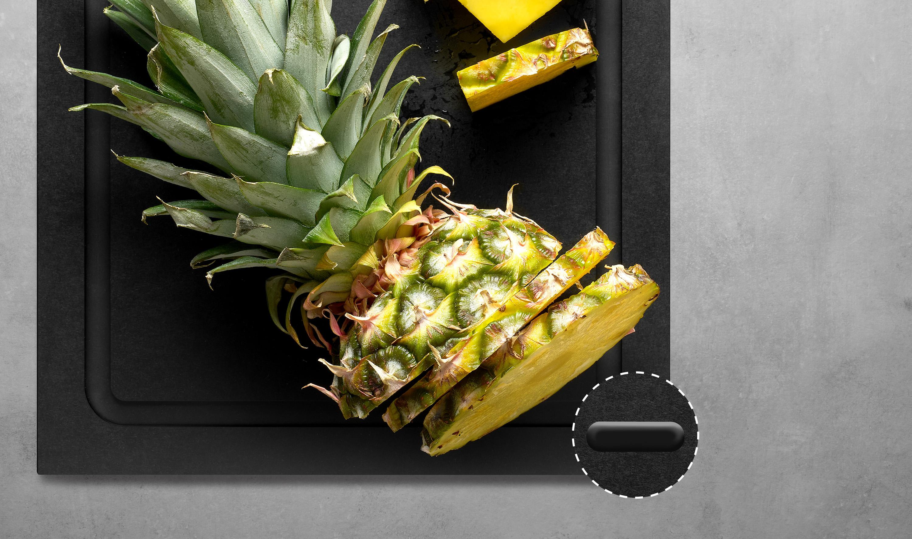 Auf dem Cut & Serve Schneidebrett mit Saftrinne liegt eine geschnittene Ananas. Die Silikonfüße der Unterseite sind zu sehen.