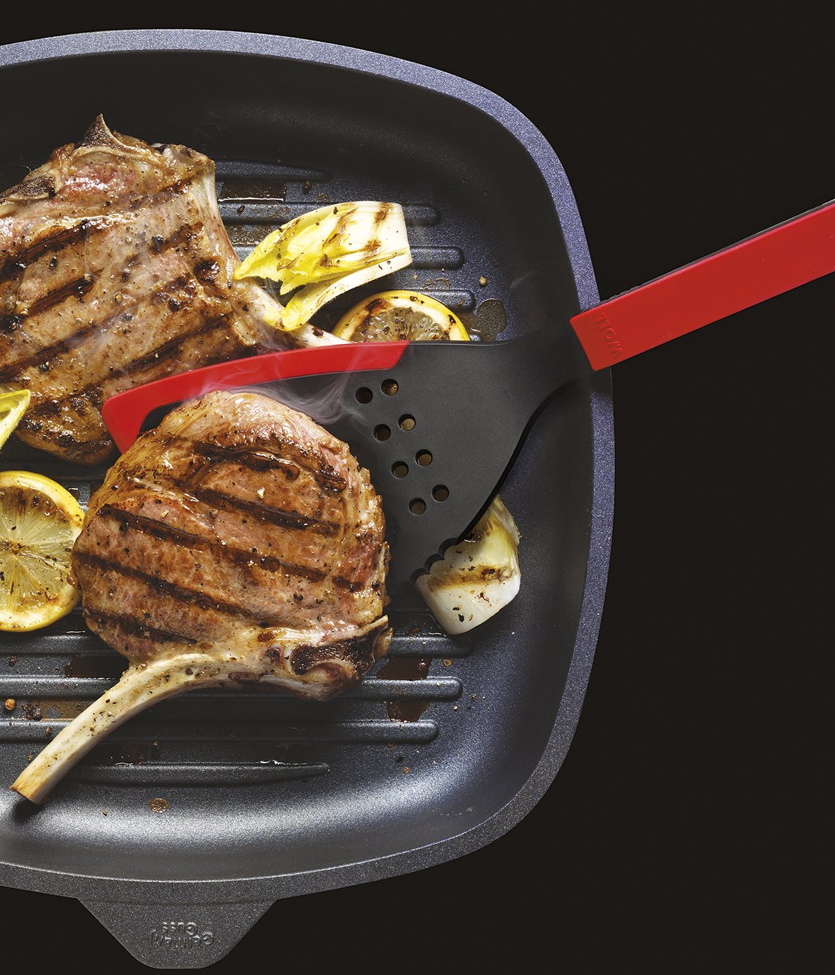 In einer viereckigen Grillpfanne werden zwei Fleischstücke angebraten und mit einem roten Cock it Jumbo Pfannenwender gewendet.