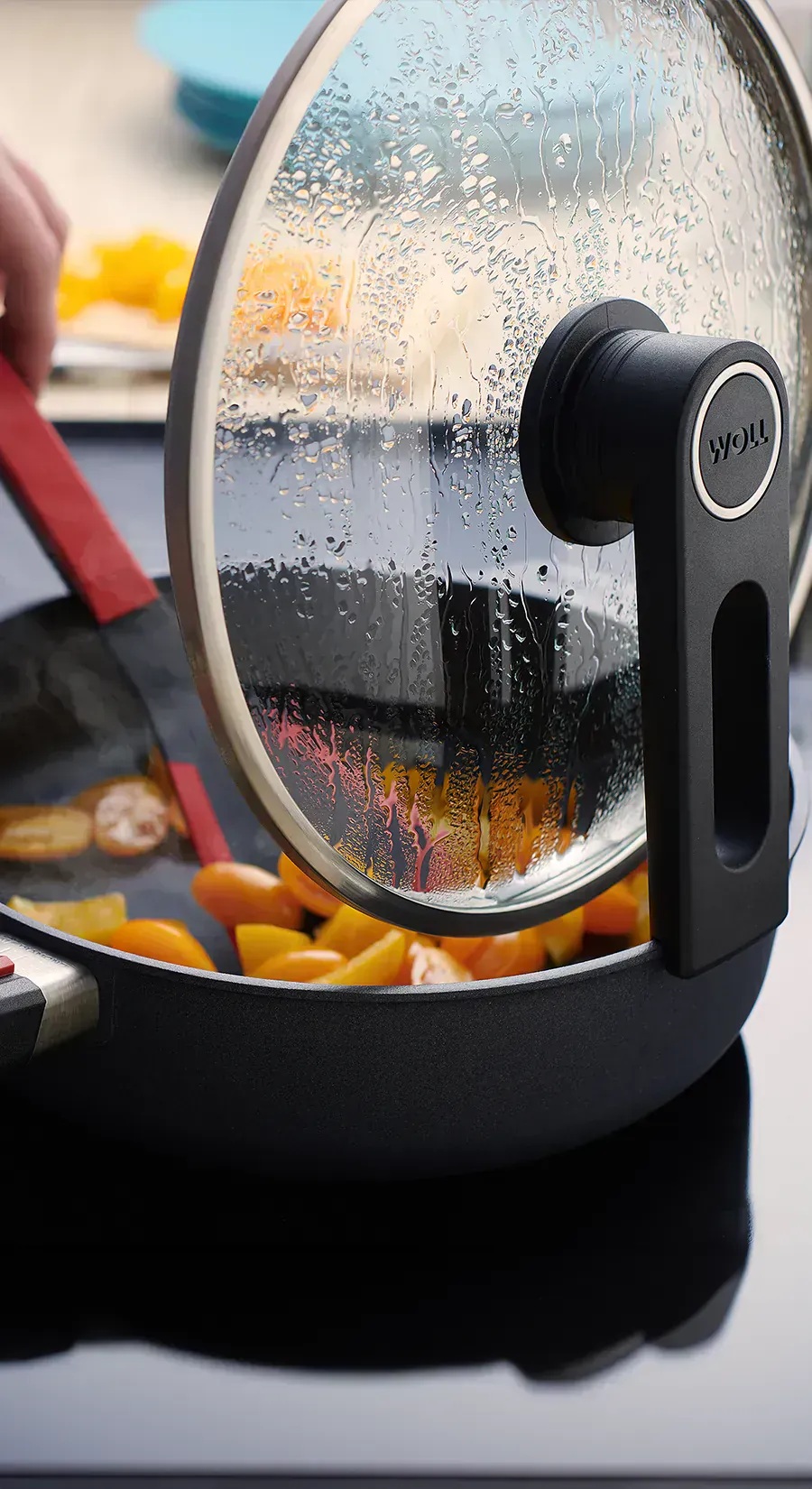 In einer heißen Diamond-Lite-Pfanne wird gerade ein dampfendes Gericht mit einem Cock-it-Pfannenwender umgerührt. Der Glasdeckel ist mit der verlängerten Seite der Smart-Lid-Serie an der Kante der Pfanne eingehängt.