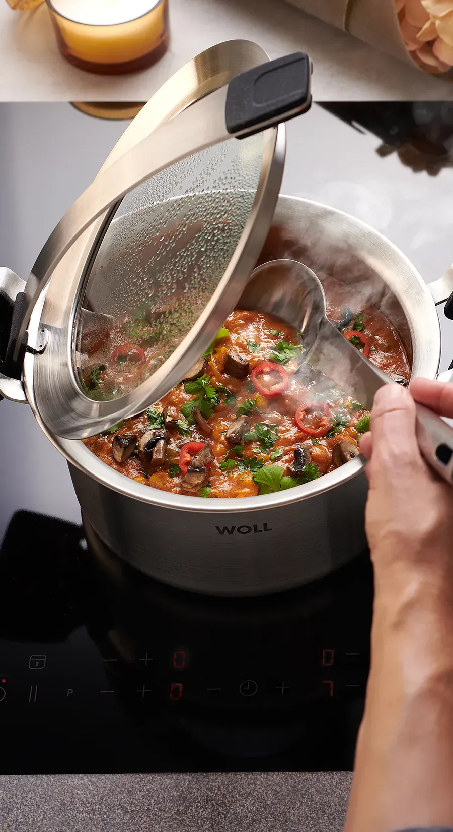 In einem runden Kochtopf der Serie „Concept Pro” wird ein dampfendes Gericht zubereitet. Der Glasdeckel wurde in den Griffeinraster gestellt, sodass er offen bleibt. So kann das Gericht mit dem Kochlöffel umgerührt werden.