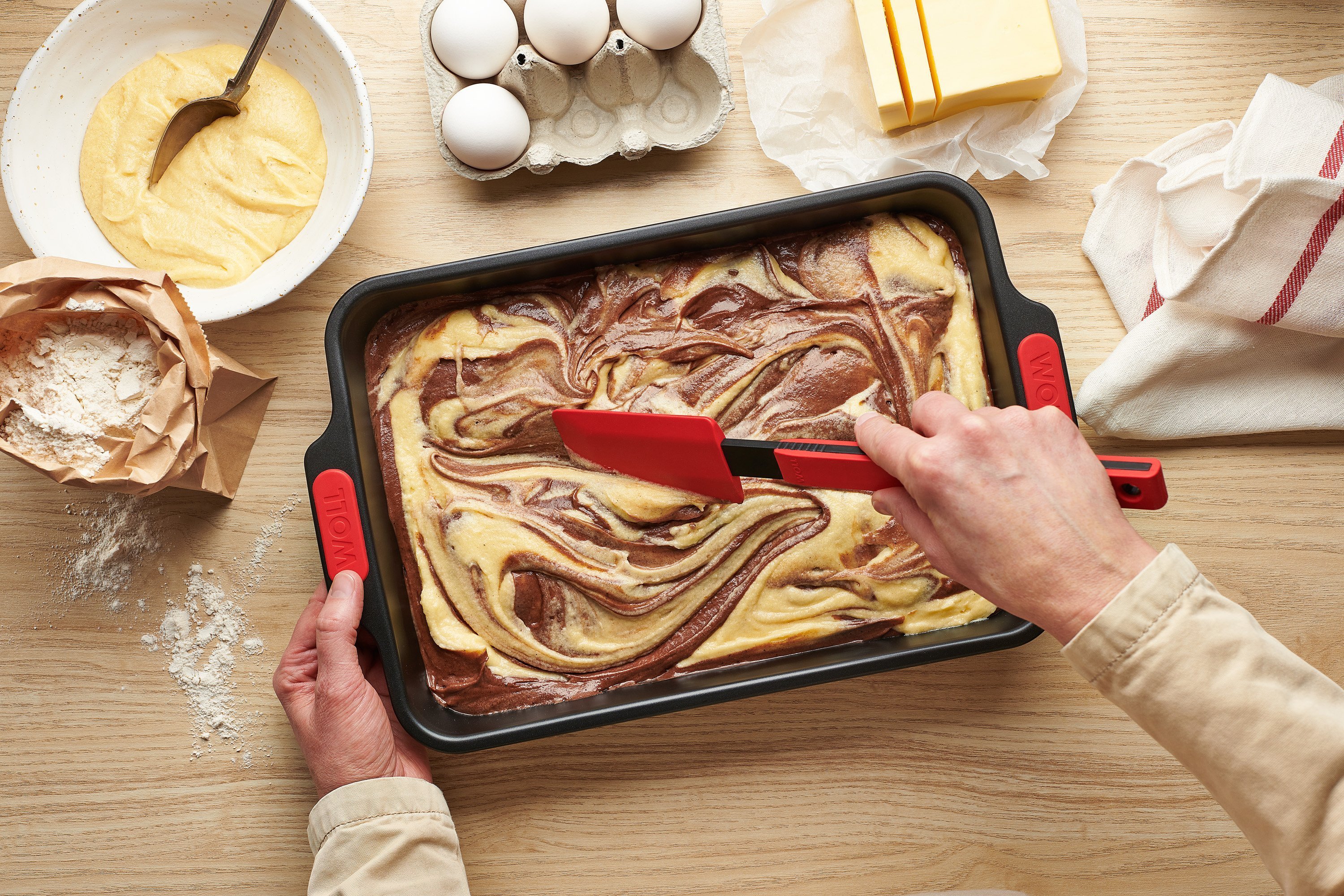In einer rechteckigen Let's bake! Backform wird mit einem Cock it Teigschaber roher Kuchenteig verteilt. 