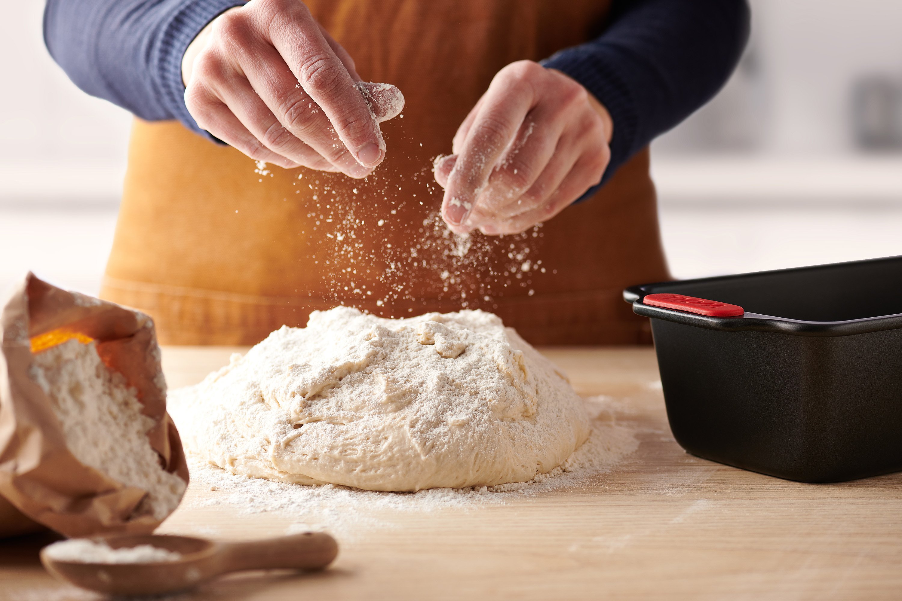 Auf der Arbeitsplatte wird Teig geknetet. Eine rechteckige Let's bake! Kastenform steht daneben.