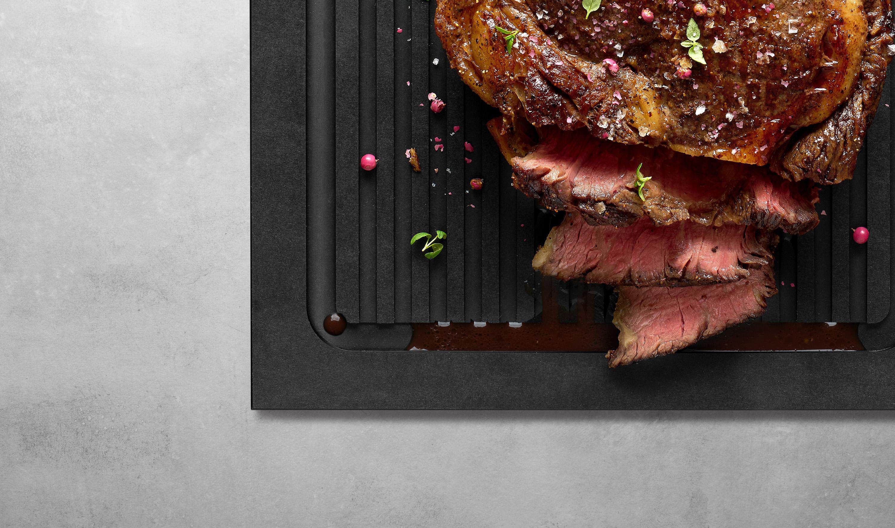 Ein Stück Fleisch wurde in Streifen geschnitten. Der dabei austretende Fleischsaft läuft in die Rillen des Cut & Serve Schneidebretts.