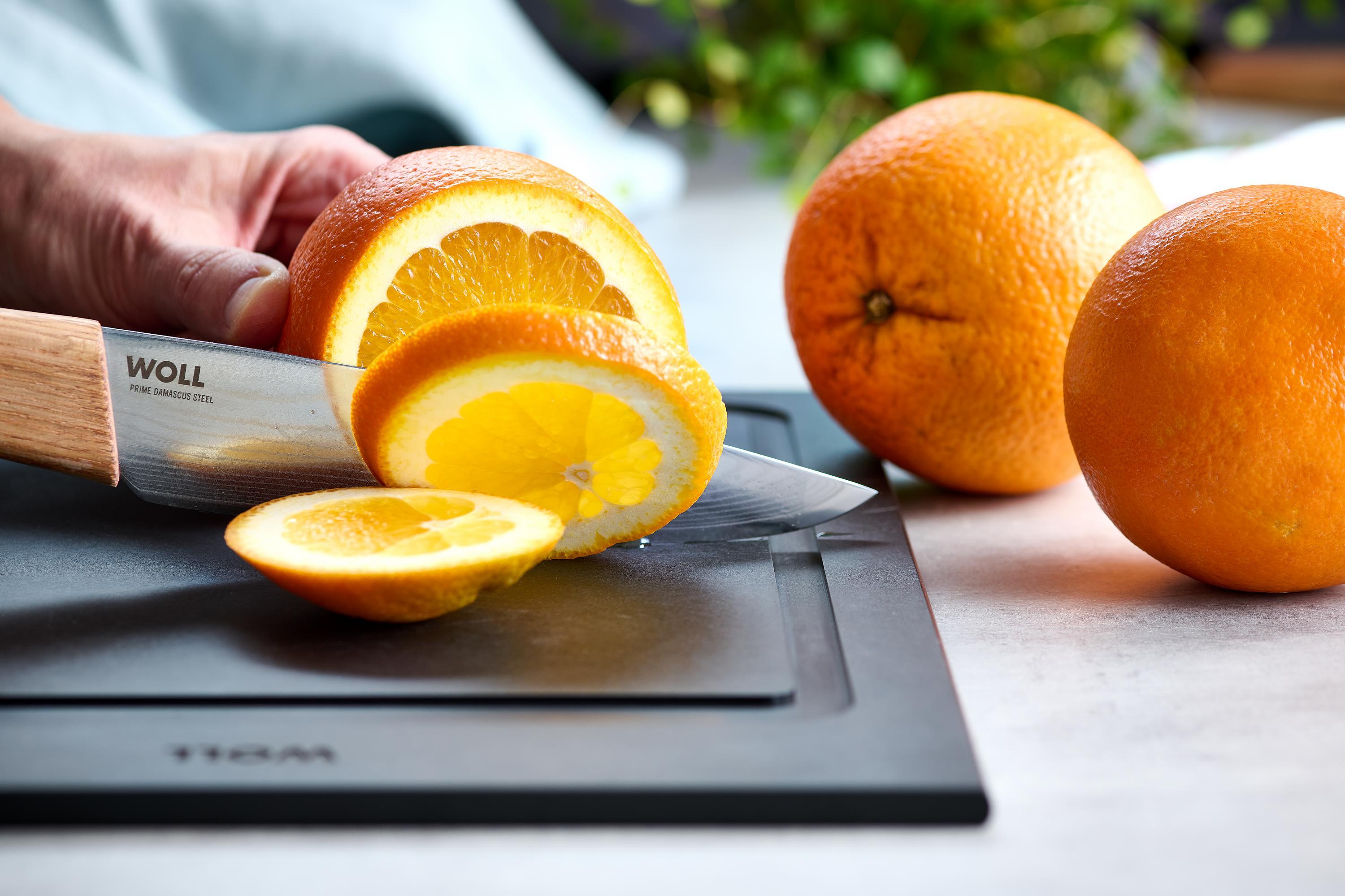 Mit dem Prime Edge Kochmesser Kompakt wird eine Orange auf einem Schneidebrett in Scheiben geschnitten. 