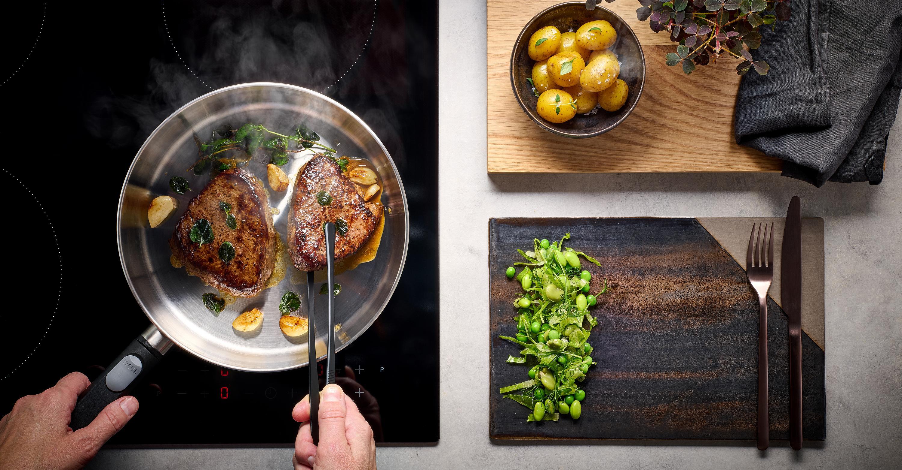 Auf dem Herd steht eine runde Logic Steel Pfanne, in der Fleisch angebraten und gewendet wird. 