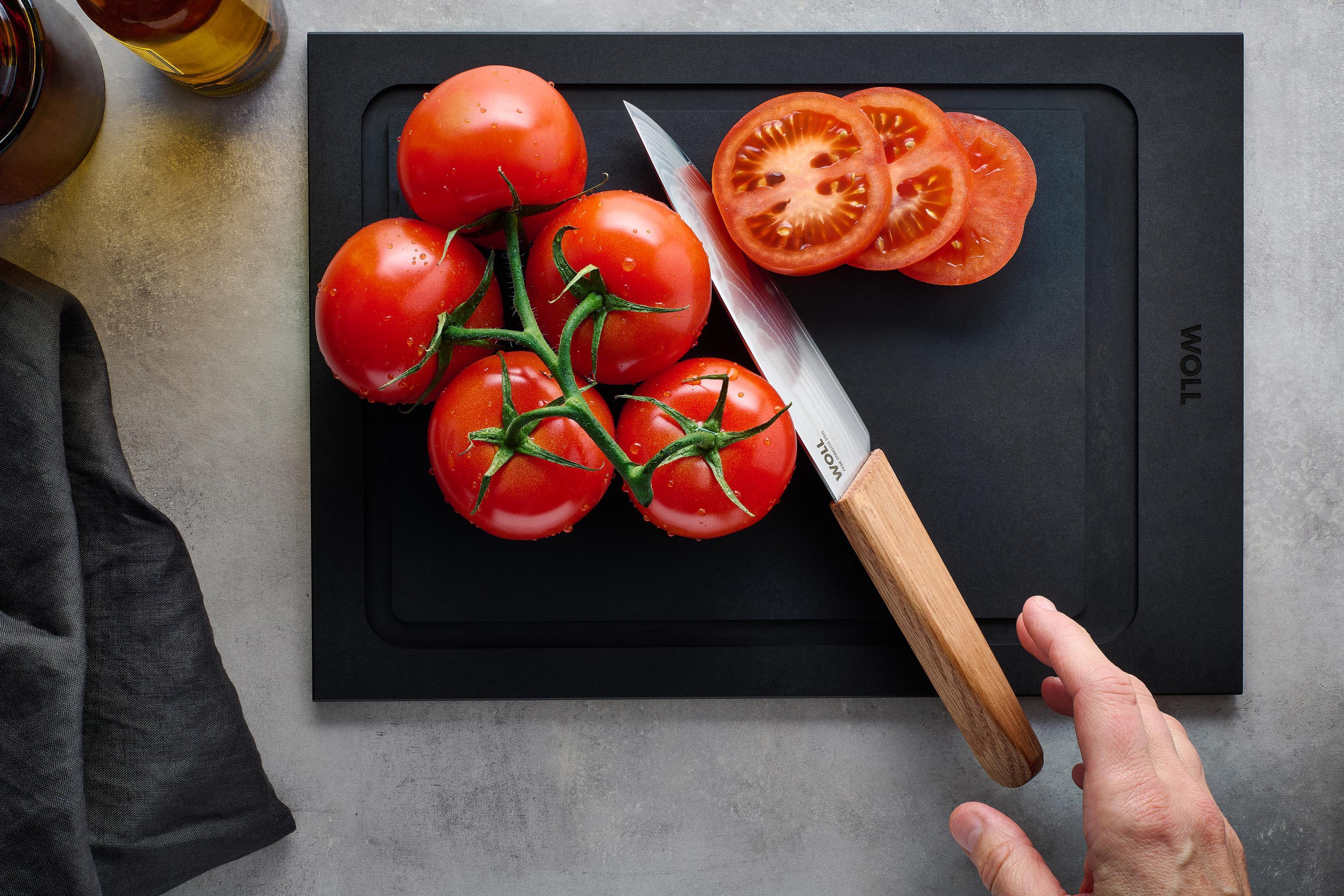 Mit dem Prime Edge Kochmesser Kompakt wird eine Tomate auf einem Schneidebrett in Scheiben geschnitten. 