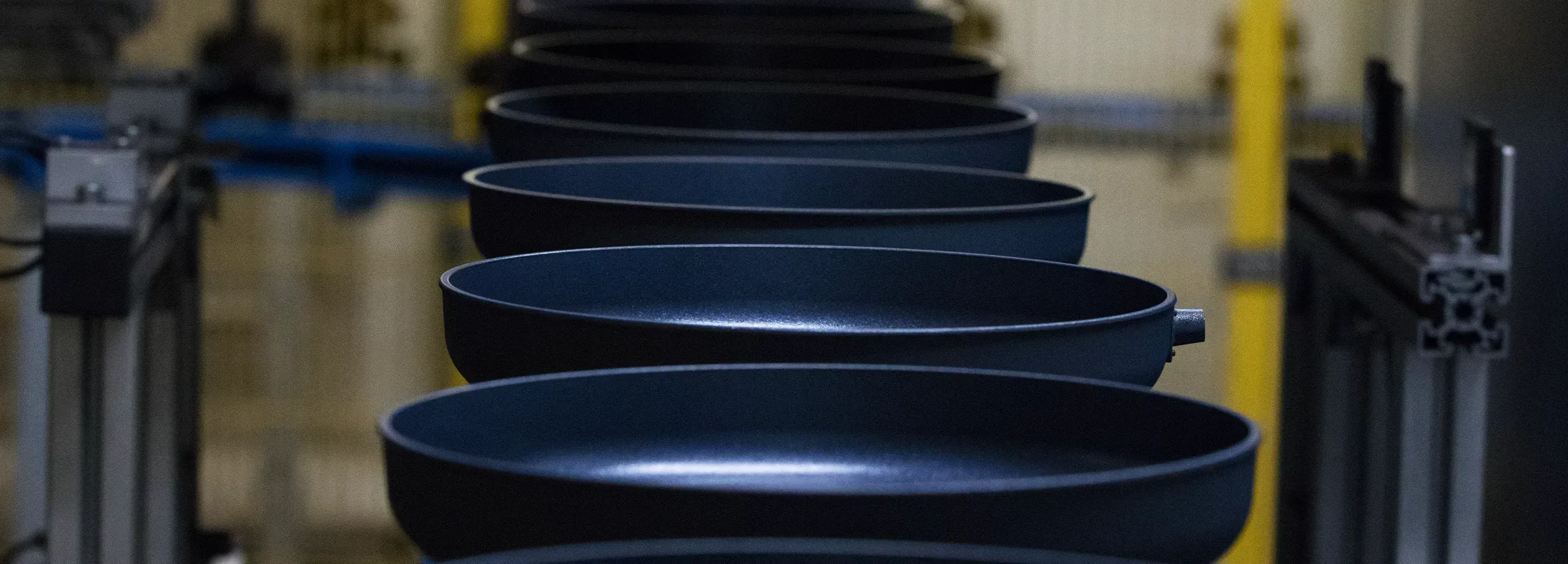 Auf dem Laufband werden mehrere beschichtete Pfannenkörper transportiert.